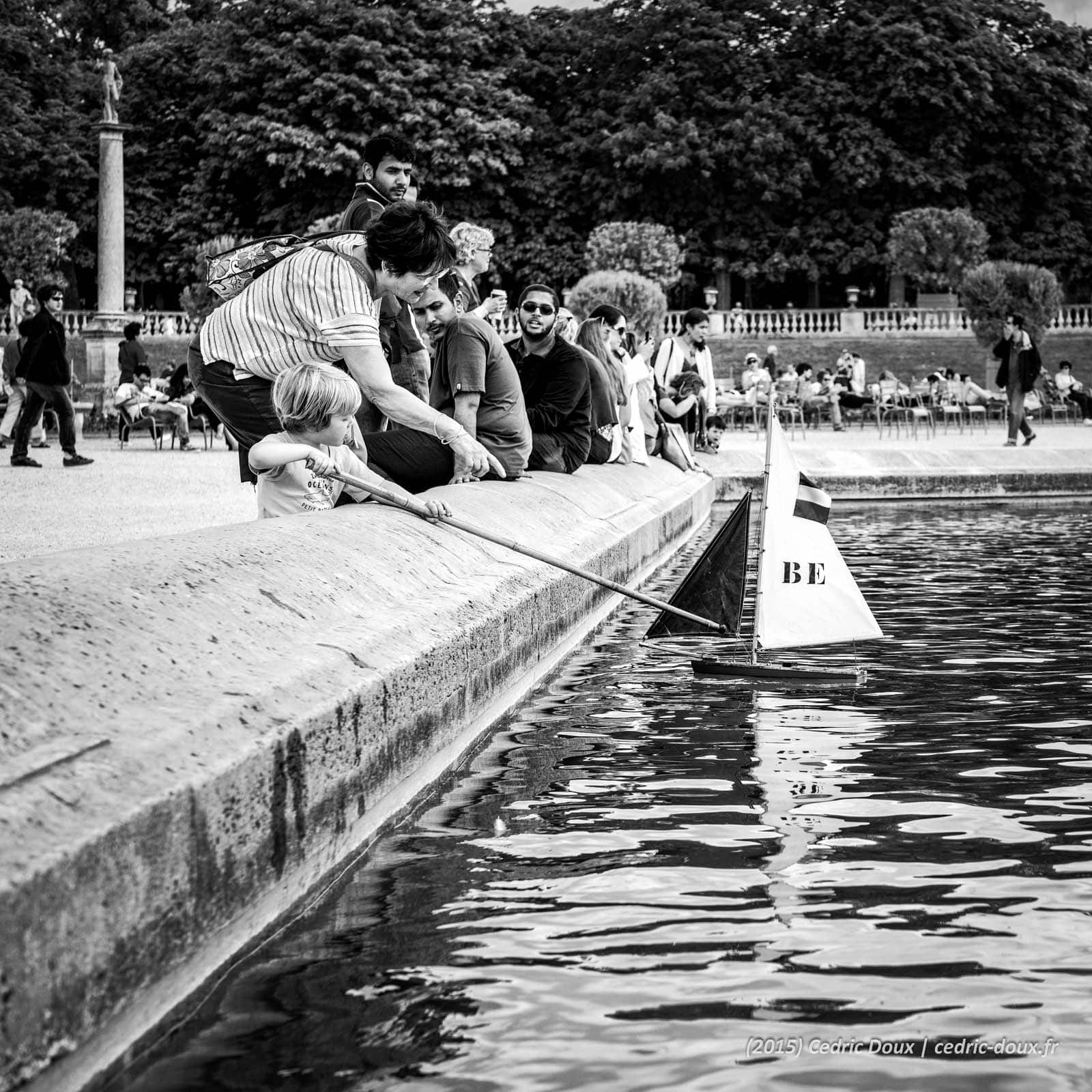 Un enfant joue avec un bateau en bois sur le plan d'eau du Jardin du Luxembourg