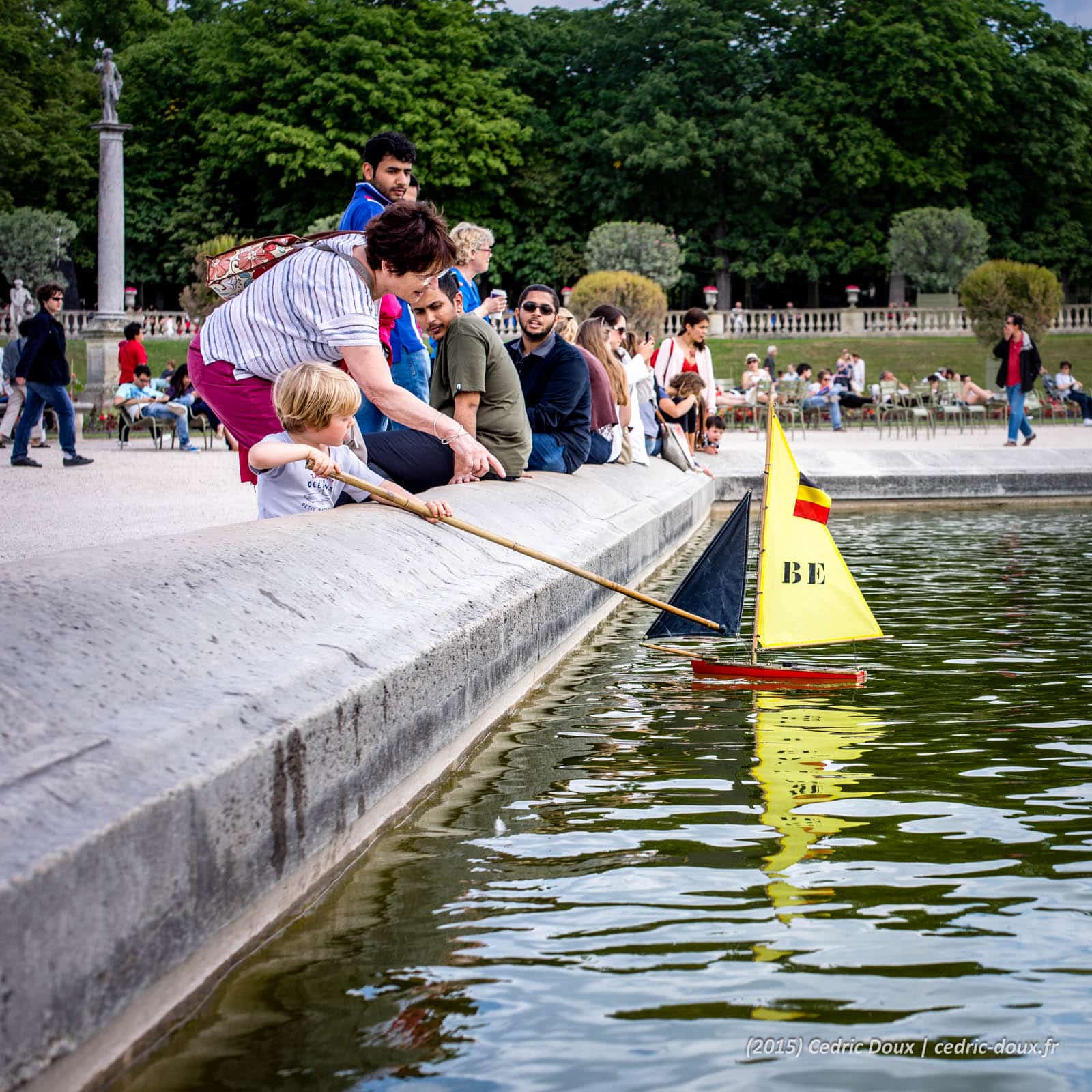 Un enfant joue avec un bateau en bois sur le plan d'eau du Jardin du Luxembourg.