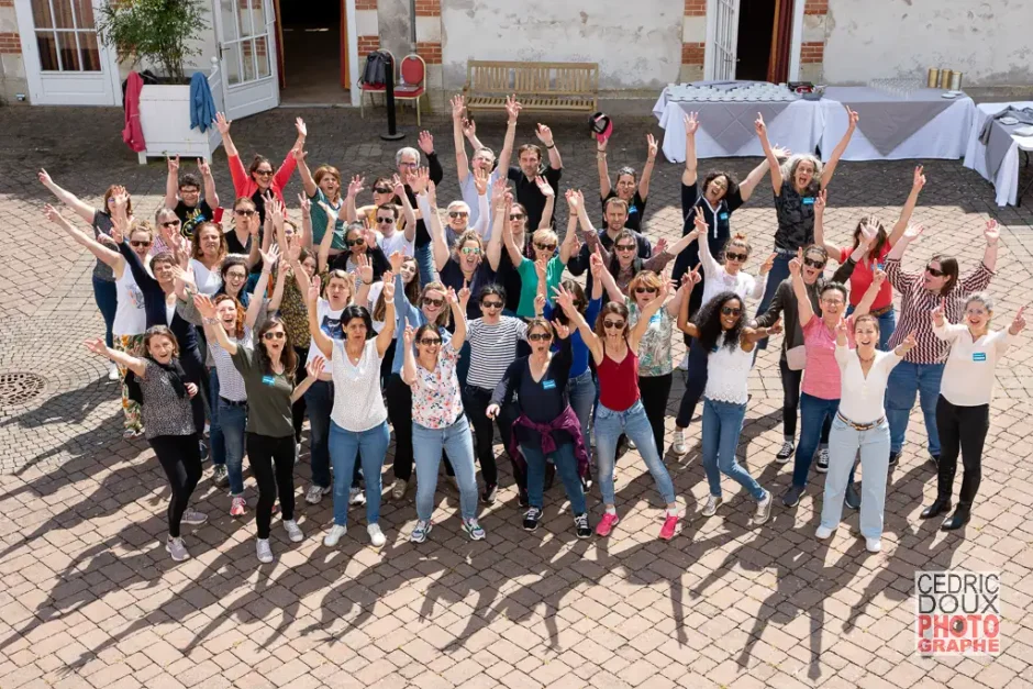 Groupe de collaborateurs réunis lors d’un séminaire d’entreprise, bras levés, exprimant la convivialité et la cohésion d’équipe en plein air