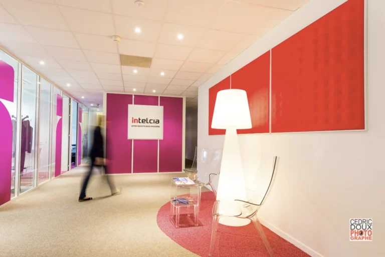 Hall d'entrée moderne avec murs rose vif, enseigne Intelcia, lampadaire design et chaise transparente